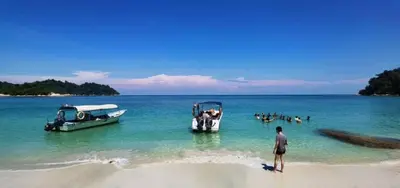 a man standing on a beach with boats in the water at HyperTribe -Pangkor Holiday Home in Kampong Sungai Udang