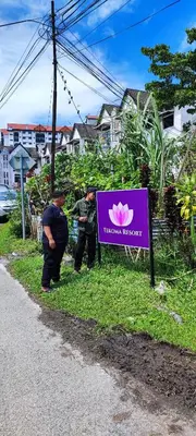 two people standing next to a sign in the grass at Tekoma Hotel & Hostel Cameron Highlands - FREE SHUTTLE SERVICE in Tanah Rata