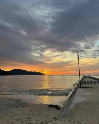 a sunset over the water with a dock on the beach at By The Sea Luxury Beachfront Resort 223 in Batu Ferringhi