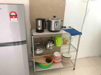 a shelf with pots and pans on it next to a refrigerator at 3 Rooms Apartment - Near Beach in Kampong Sungai Udang