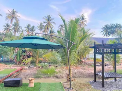 a blue umbrella and a bench and palm trees at Homestay Naim Sabak Bernam in Sabak Bernam