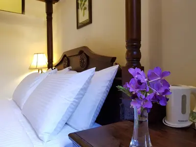 a bed with a vase of purple flowers on a table at Betel Nut Lodge in George Town