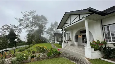 a white house with a porch with flowers and plants at Bukit Ruil Bungalow - Clementine Suite in Tanah Rata
