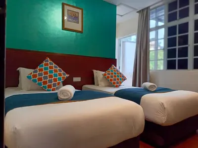 three beds in a room with a green wall at Beautiful Marigold Hotel in Tanah Rata