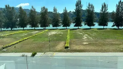 a large grass field with trees and water in the background at Grand’e La Villa Homestay in Lumut