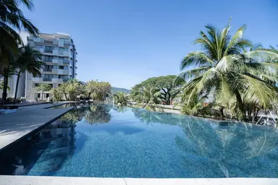 a swimming pool with palm trees and a building at Batu Ferringhi By The Sea Luxurious 2BR Suite 6 Pax in Batu Ferringhi
