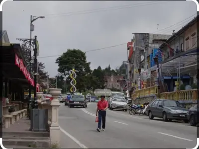 a man walking down a city street with cars at Hillside cottage chalet studio in Tanah Rata