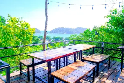 a table and benches on a deck with a view of the water at Woodcookies Guesthouse in Pangkor