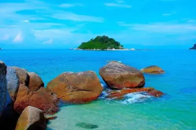 a group of rocks in the water with an island in the background at De Clinique Hotel in Pangkor