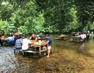 a group of people sitting at a picnic table in a river at RS Homestay Gerik in Gerik