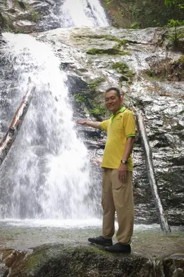a man standing on a rock in front of a waterfall at Orchard Lake House - Entire bungalow, 4 rooms, 9 beds, 13 persons in Behrang Hulu