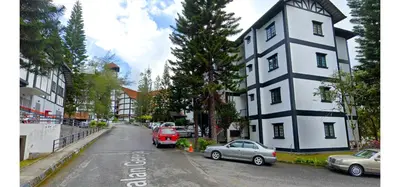 a street with cars parked in front of a white building at Cozy Cottage-Style Apartment Entire Unit in Tanah Rata