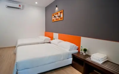 two beds in a bedroom with an orange accent wall at Big Orange Hotel Sungai Petani in Sungai Petani