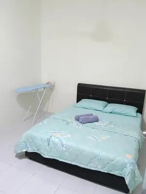 a bed with a blue comforter and a table at The Welcome Mat Homestay in Seri Iskandar