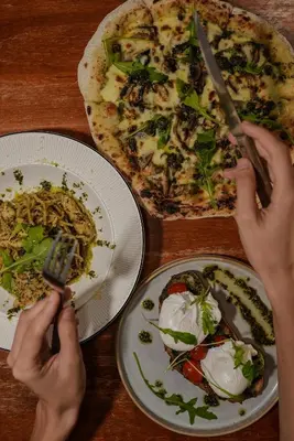 a person cutting a pizza on a table with plates of food at Moustachz Hauze , Georgetown in George Town