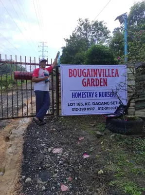 a man standing next to a fence with a sign at Bougainvillea Garden KKB in Kuala Kubu Baharu