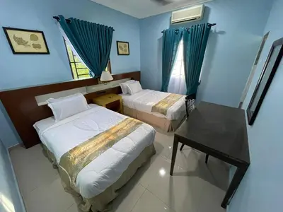 a bedroom with two beds and a desk and a window at NHR Harmoni in Simpang Ampat