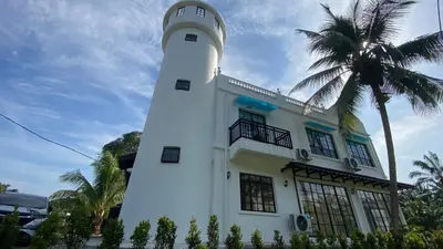 a lighthouse in front of a building with a palm tree at Pearl Castlestay in Tanjung Karang