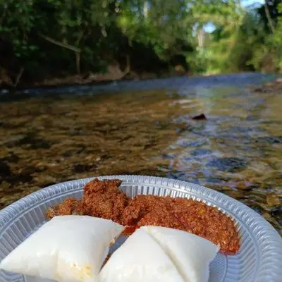 a piece of food on a plate on a table near a river at MKF Homestay Padang Stang, Gerik in Gerik