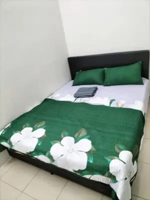 a bed with a green blanket with white flowers on it at AMRI KLATE Homestay in Seri Iskandar