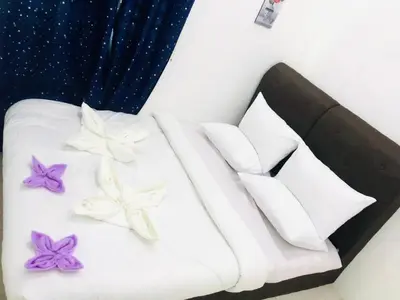 a bed with white pillows and purple flowers on it at Syapins Cozy Haven Lunas Homestay Musslim Only in Lunas