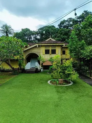 a yellow house with a yard with green grass at Bagas Zakariah Orchard Lodge in Gopeng