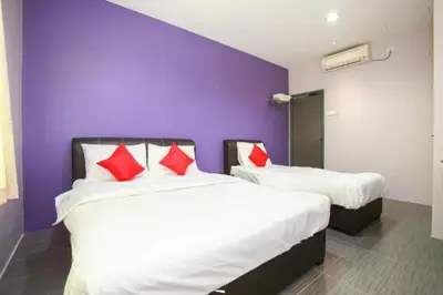 two beds in a room with purple walls and red pillows at De Hotel in Teluk Intan