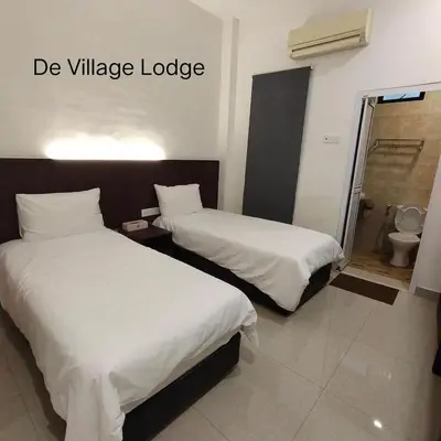 two beds in a hotel room with white sheets at De Village Lodge in Balik Pulau