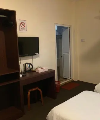a hotel room with a bed and a desk with a television at De Village Lodge in Balik Pulau