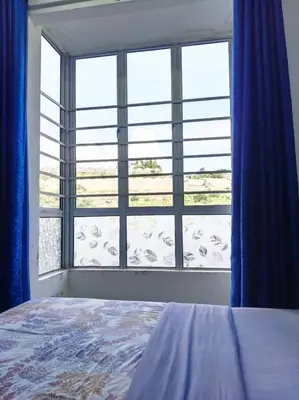 a bedroom with a large window with blue curtains at IRDINA HomestayMuslim's 2 at Emerald Avenue Brinchang Centrum in Brinchang