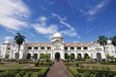 a large white building with palm trees in front of it at Ipoh Kinta Riverfront Air-Con Cozy Home in Ipoh