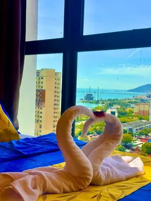 two swans sitting on a bed in front of a window at Deluxe Suite for10 Stunning Sea &City ViewsNetflix in Jelutong