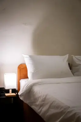 a bed with white sheets and a lamp on a table at Aayu Pantai - George Town, Penang in George Town