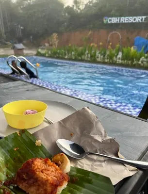 a table with a plate of food and a swimming pool at CBHResort Agrofarm in Kampong Benchah Tualang