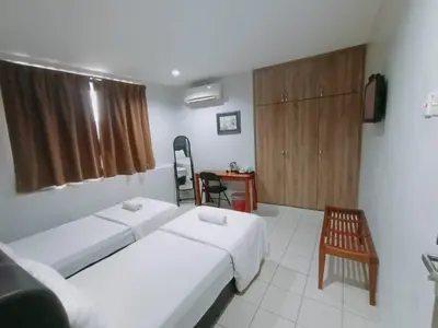 a room with two beds and a chair and a table at Reintree Lodge Hotel Ipoh in Ipoh