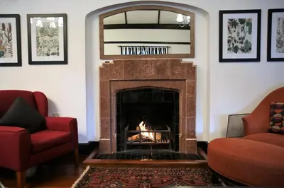 a living room with a fireplace with two red chairs at Bukit Lowick Bungalow in Tanah Rata