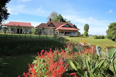 a house with a garden with flowers in front of it at Bukit Lowick Bungalow in Tanah Rata