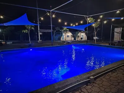 a blue swimming pool at night with a marquee at Dome Glamping Lojing Highlands in Ladang Pangoi
