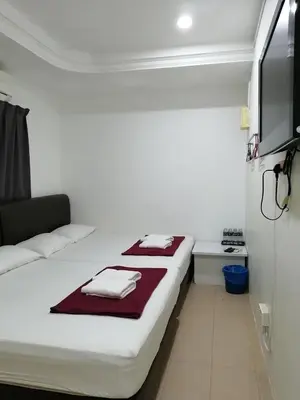 a white room with two beds and a flat screen tv at Rasa Motel in Batu Ferringhi