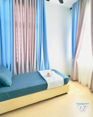 a bed in a room with blue and pink curtains at Homestay AZ Kulim in Kulim