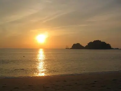 a sunset over the ocean with a beach and an island at Nipah Bay Villa in Pangkor