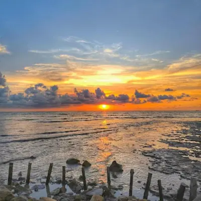 a sunset on a beach with the ocean at Quadruple Traditional Wooden GuestHouse in Balik Pulau