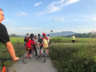 a group of people riding bikes down a dirt road at Quadruple Traditional Wooden GuestHouse in Balik Pulau