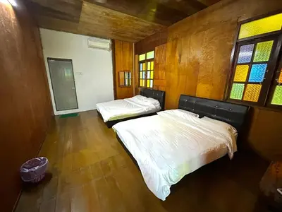 two beds in a room with wooden walls and windows at Quadruple Traditional Wooden GuestHouse in Balik Pulau