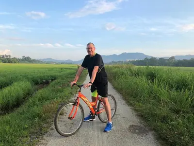 a man standing next to a bike on a dirt road at Junior Suite Nature of Penang Guesthouse in Balik Pulau