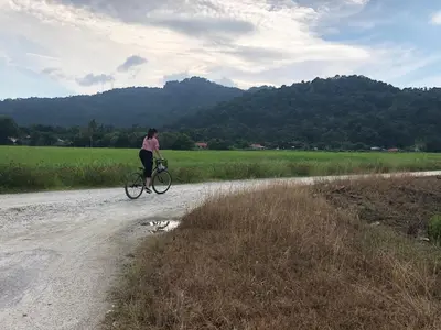 a woman riding a bike down a dirt road at Tatami Room Malay Wooden Stay in Balik Pulau