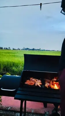 a grill with food cooking on it next to a field at Akira Laman Padi Tg Karang in Tanjung Karang