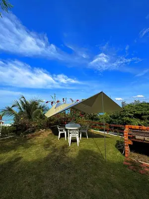 a table and chairs under an umbrella in the grass at VELAMUNDi INN Batu Ferringhi in Batu Ferringhi