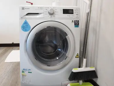 a white washing machine with a broom next to it at The Tiny Treasure Stay #1BR in George Town