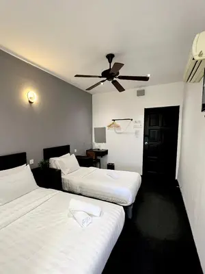 two beds in a hotel room with a ceiling fan at Quee Hotel in George Town